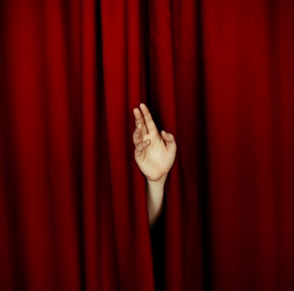 Hand peeking through red curtains