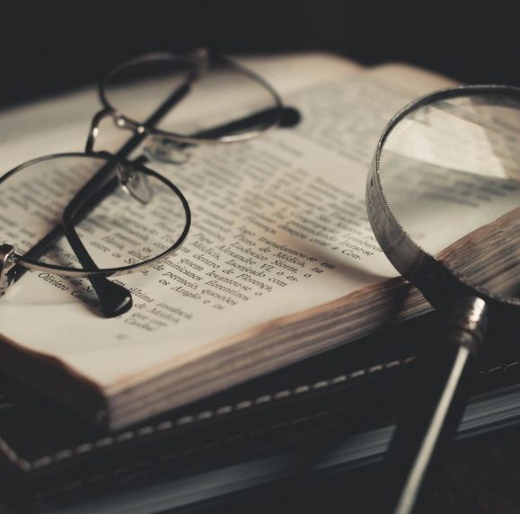 Open book with glasses resting on top and magnifying glass