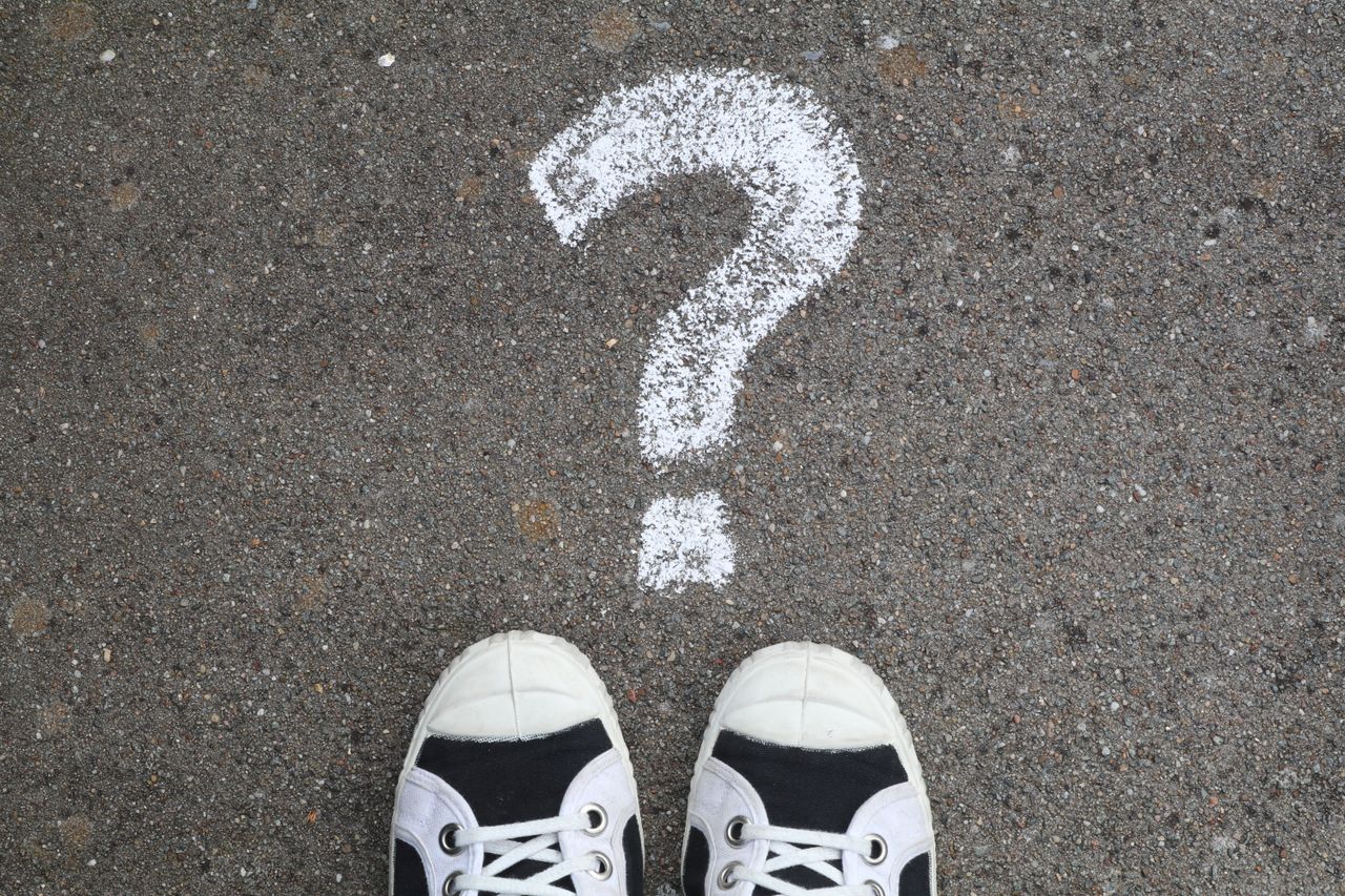 Question mark written in chalk with black and white trainers standing underneath