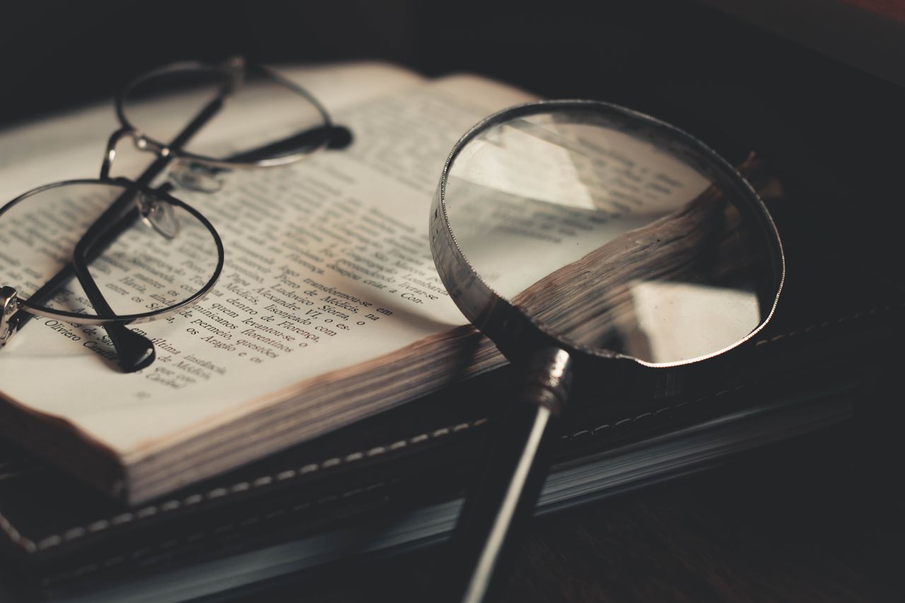 Open book with glasses resting on top and magnifying glass