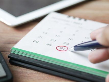 Close-up shot of a hand marking a date on a calendar with a pen, emphasizing planning and scheduling.
